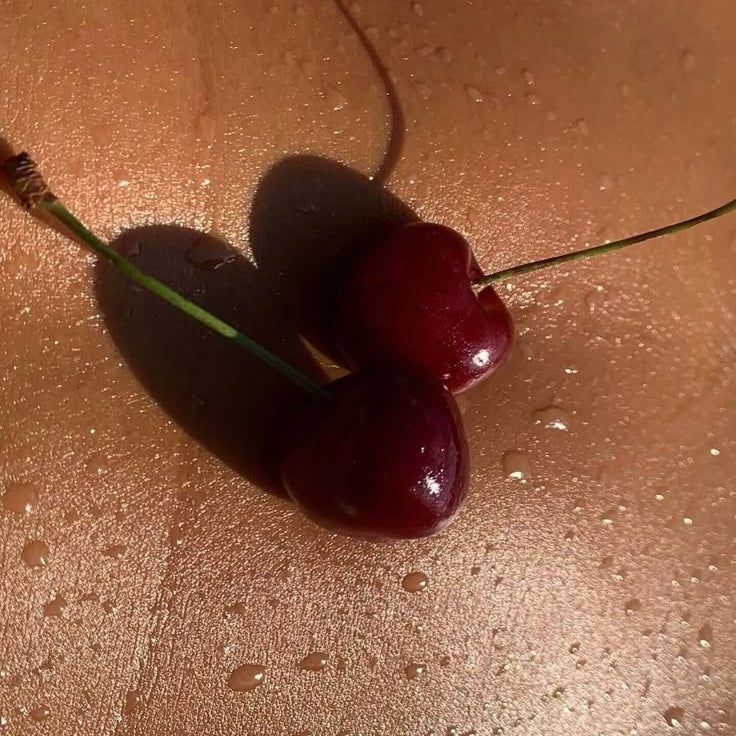 Two cherries on a reflective surface with water droplets.